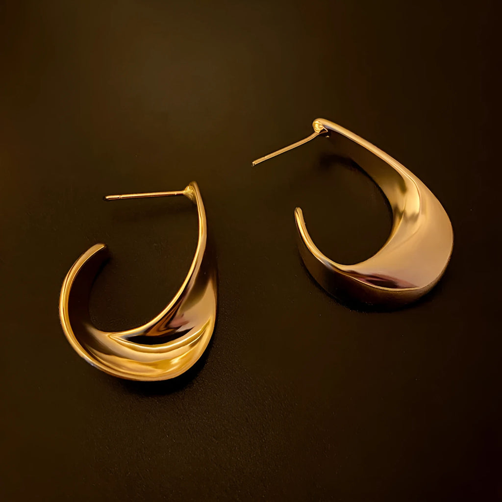 A pair of geometric twisted metal earrings with a round shape in a gold colour.
