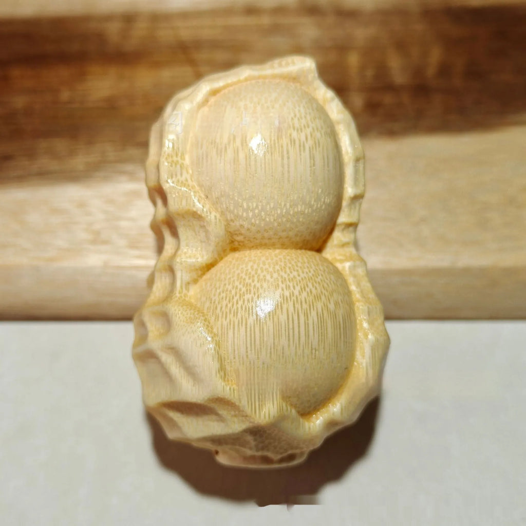 Solid natural bamboo ornament carved into a peanut shape on a plain background.