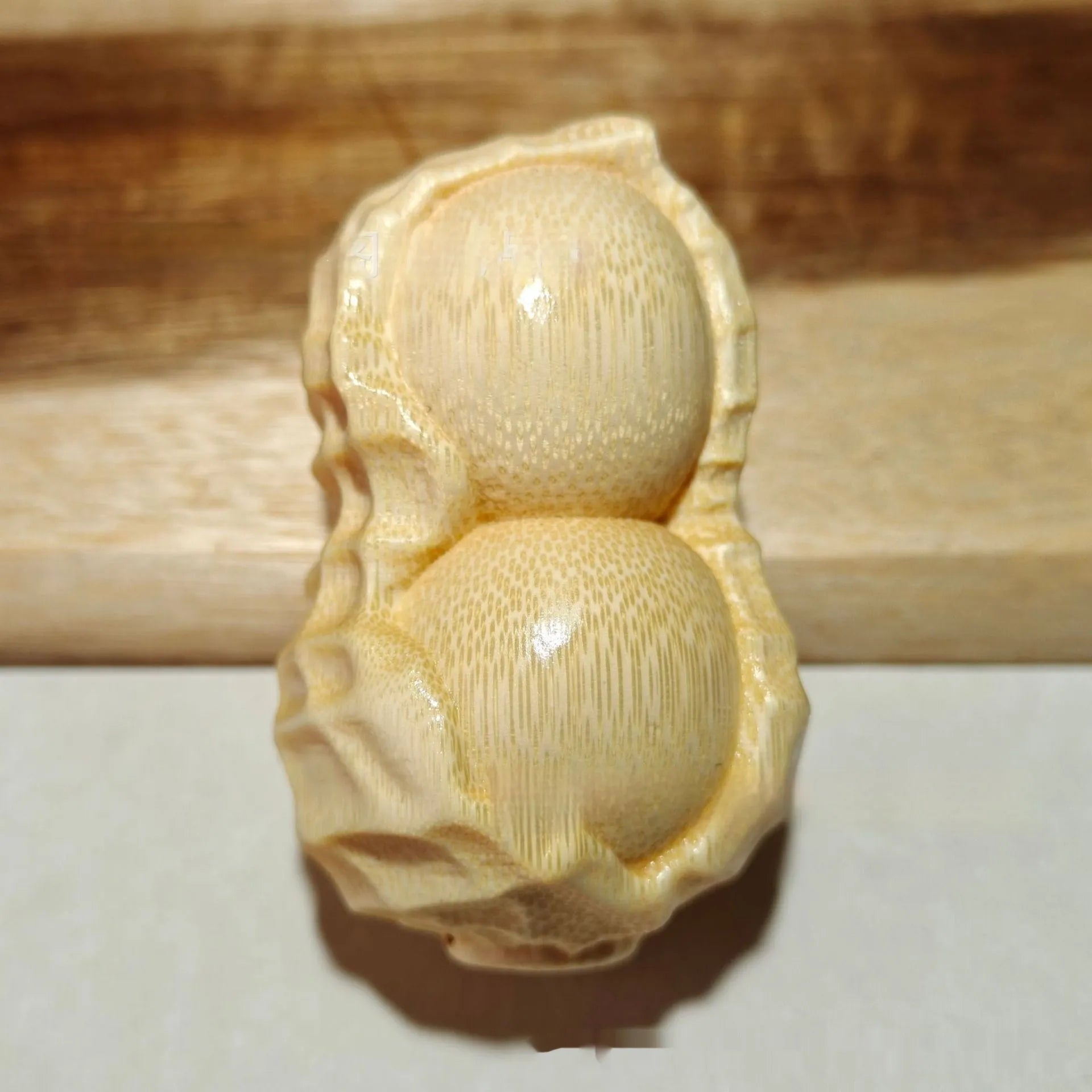 Solid natural bamboo ornament carved into a peanut shape on a plain background.