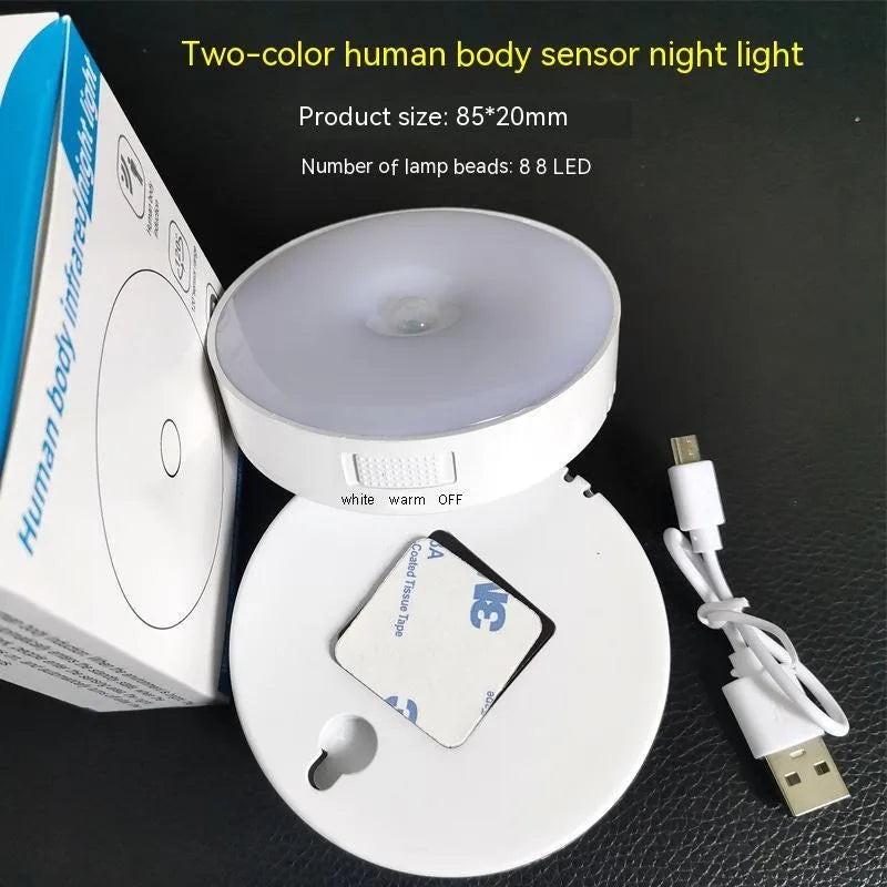 Small white circular motion sensing LED night light with adhesive backing next to a USB charging cable.