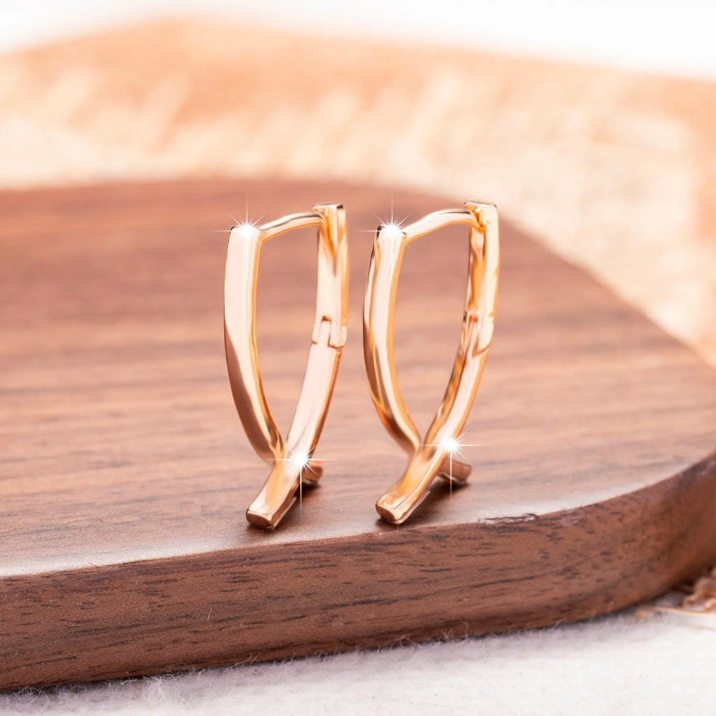 A pair of rose gold coloured cross shaped earrings on a plain background.