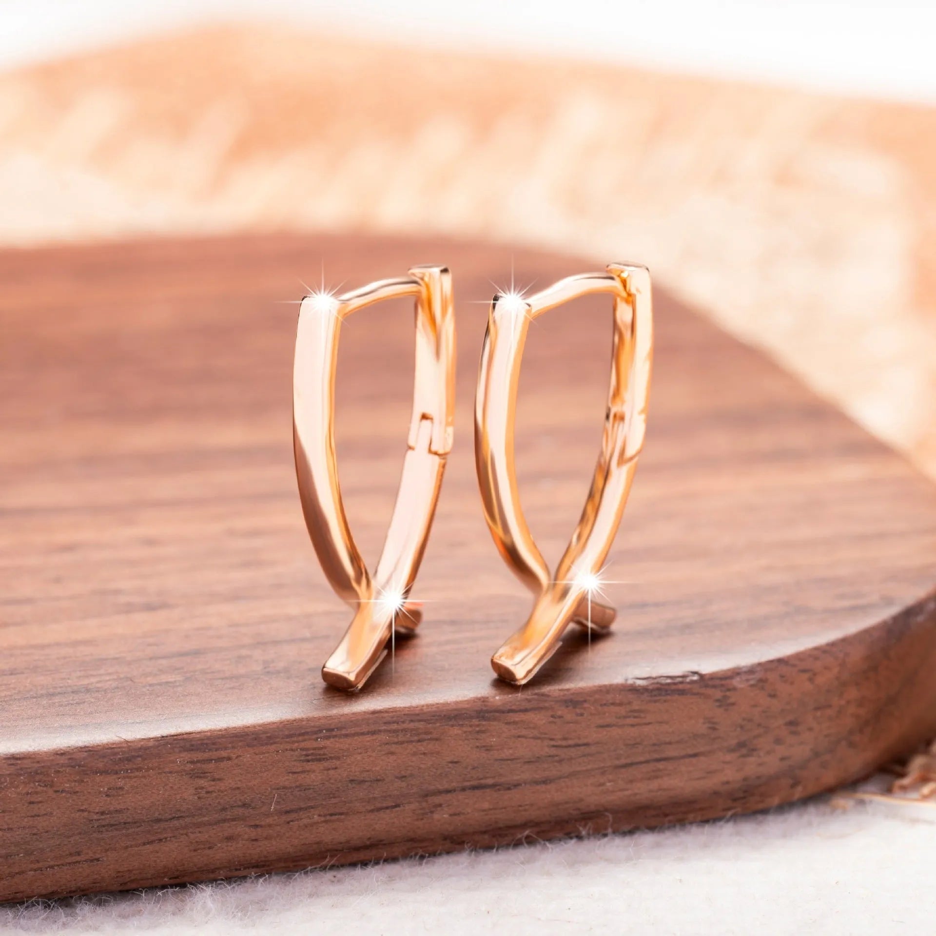 A pair of rose gold coloured cross shaped earrings on a plain background.