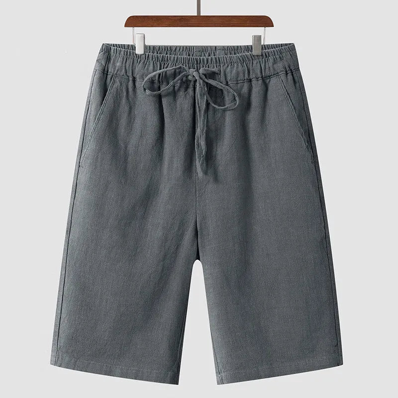 Men's beige linen casual shorts with a loose fit and cropped length on a plain background.