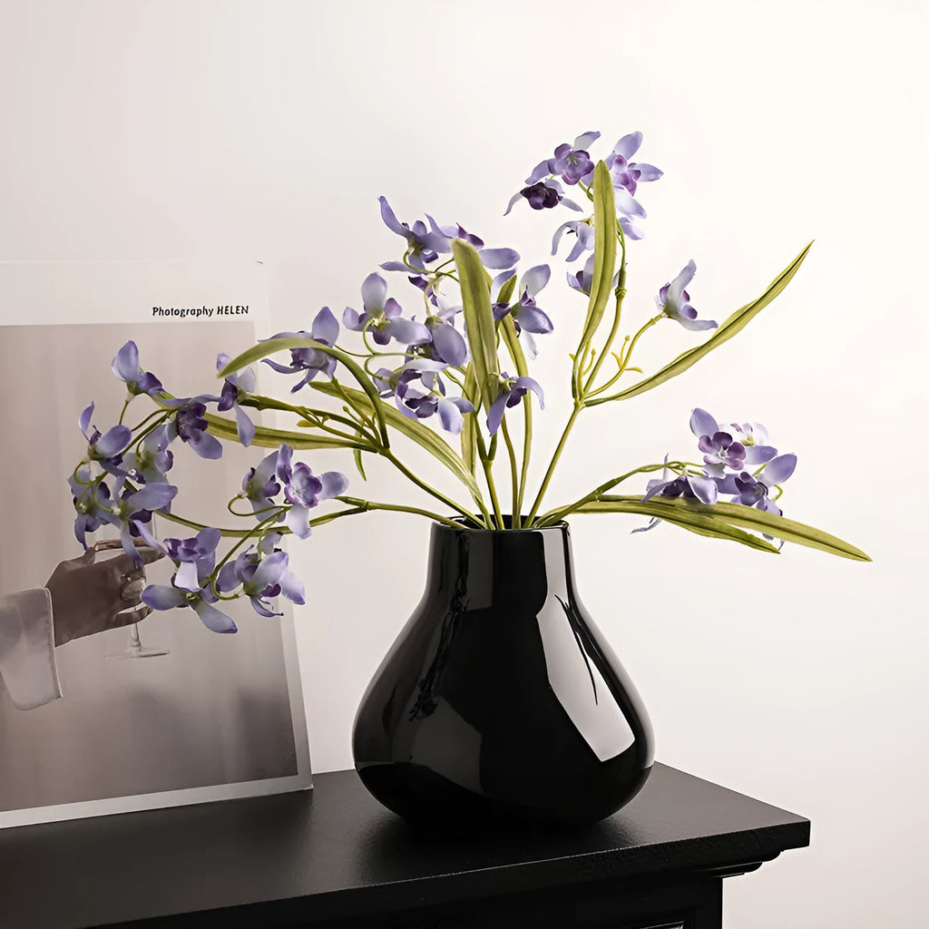 Ceramic decorative vase with coloured glaze surface and artificial orchid flowers in black or white colour