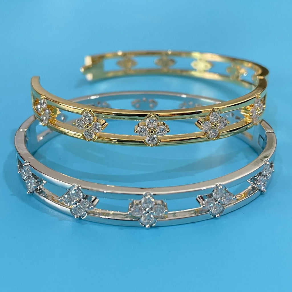 Gold and silver women's hollow bracelets with zircon stones and four-leaf clover charms on a white background.