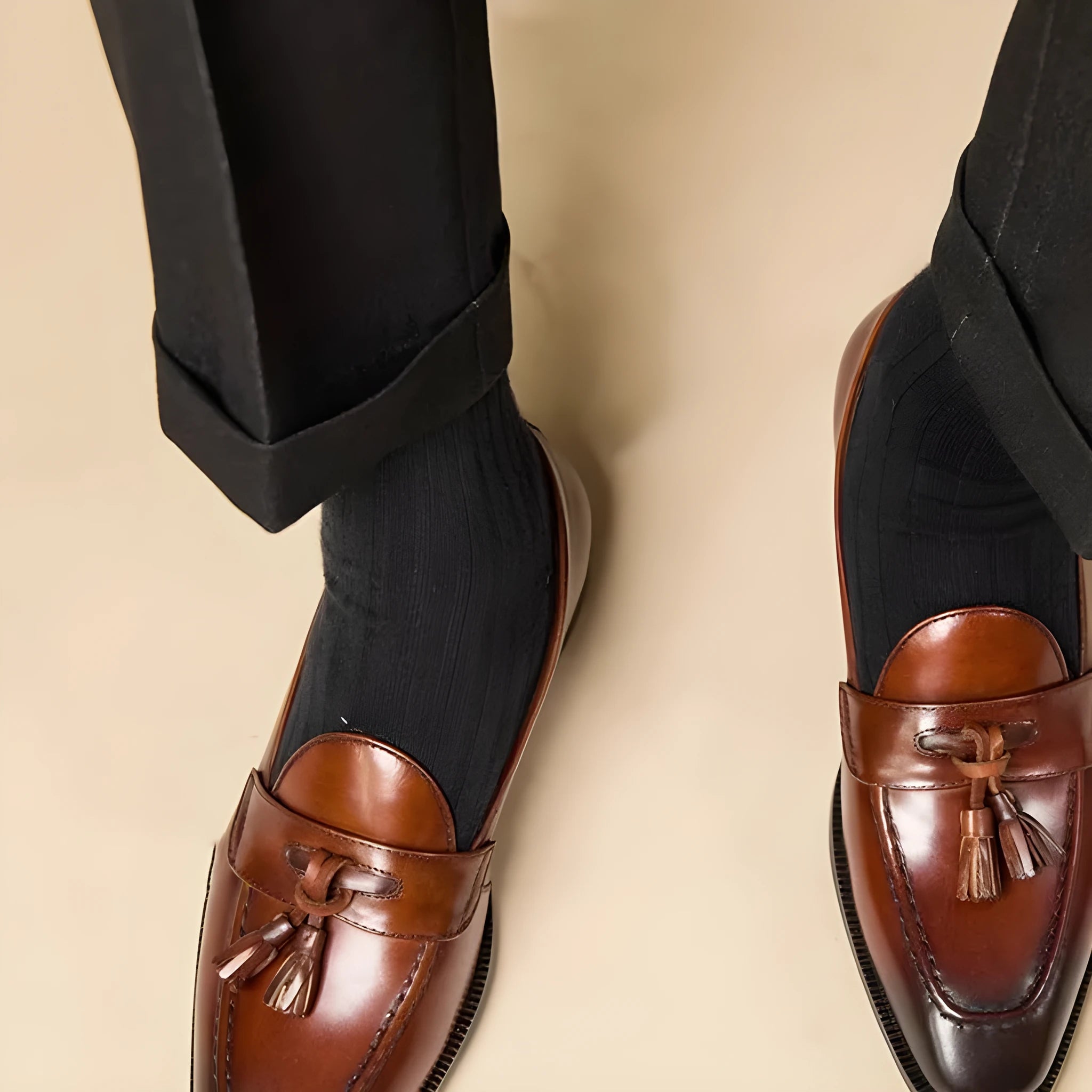 Men's black polished leather tassel loafers with a rubber sole on a white background.