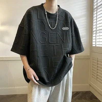 Man wearing a grey loose-fit T-shirt with a raised 3D retro letter print on the front.