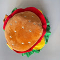 A cat wearing a soft cotton cartoon hamburger headdress with an adjustable neck strap.
