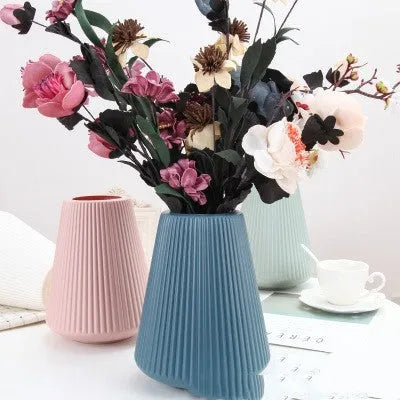 Simple plastic decorative flower vase in blue, green, pink, or white on a desktop.