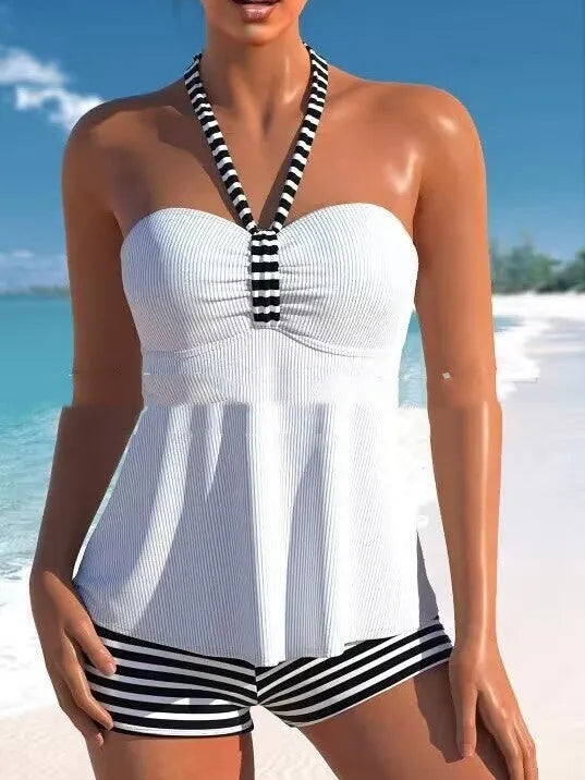 Woman modelling a black and white striped off-shoulder one-piece swimsuit on a beach.