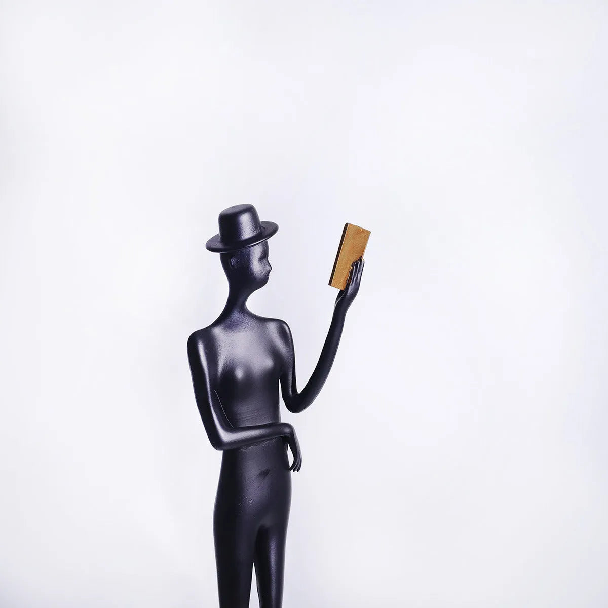 Black metal sculpture of a seated woman reading a book, modern minimalist desk decor.
