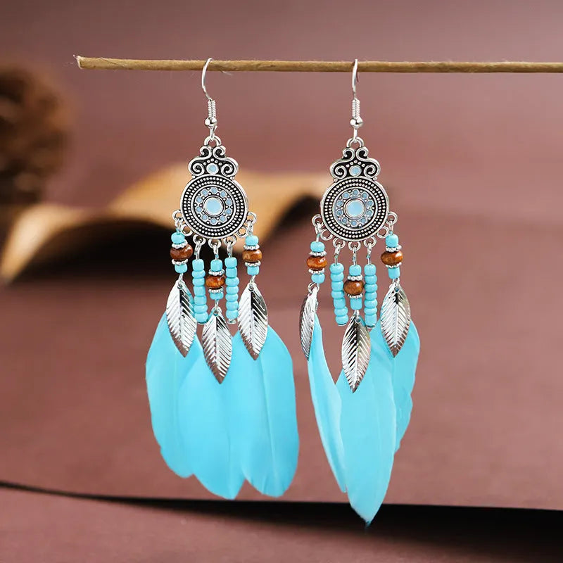 Close-up of a pair of bohemian-style feather and leaf design drop earrings in alloy, showing the electroplated finish.