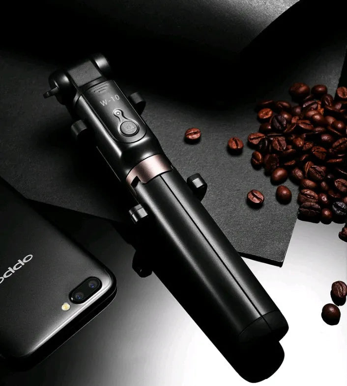 Aluminium Bluetooth selfie stick with tripod base and remote control next to a smartphone.