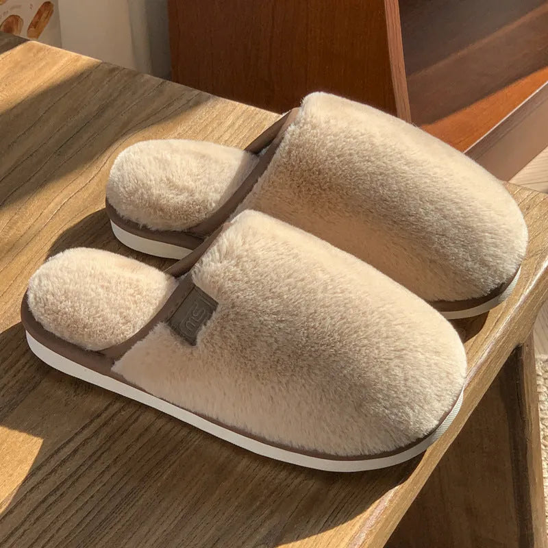 Pair of solid colour plush house slippers with PVC sole on a wooden floor.