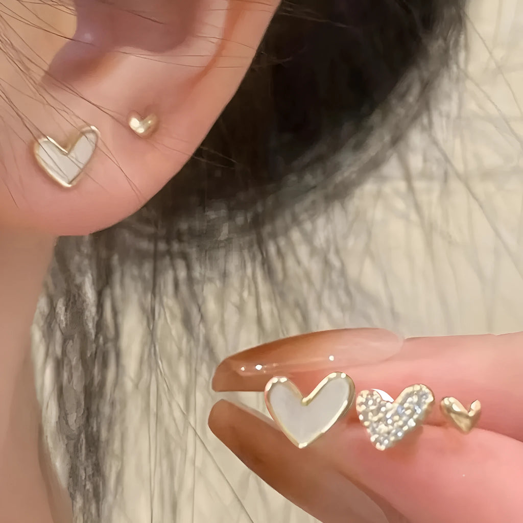 Three pairs of women's heart-shaped alloy earrings in gold, black, white, and pink colours