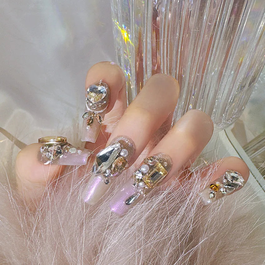 Ten false nail patches with rhinestones on a card, next to jelly adhesive and manicure tools.
