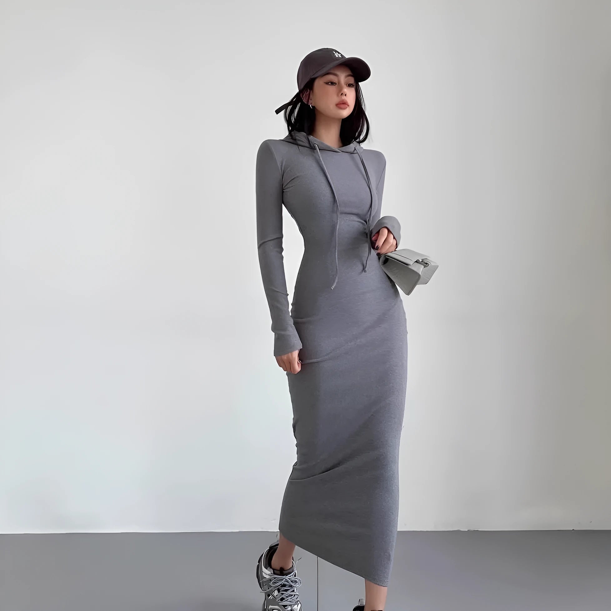 A woman wearing a light grey hooded sheath dress with long sleeves, showcasing the high waist and over-the-knee length.