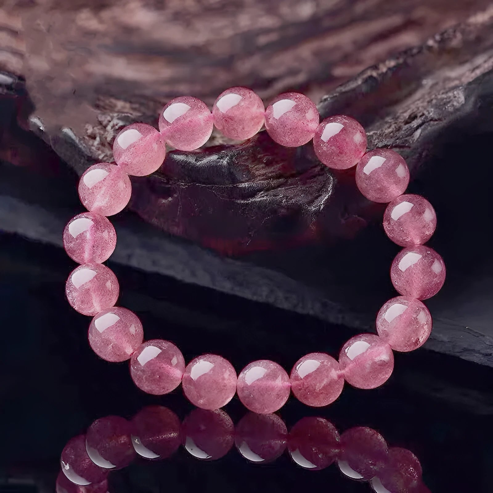 Women's strawberry quartz crystal bracelet with polished round beads on a white background.