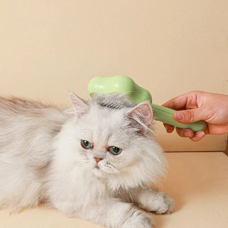 Green and yellow self-cleaning cat grooming comb with stainless steel needles on a white background.
