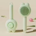 Green self-cleaning cat brush with metal comb and release button for pet grooming.
