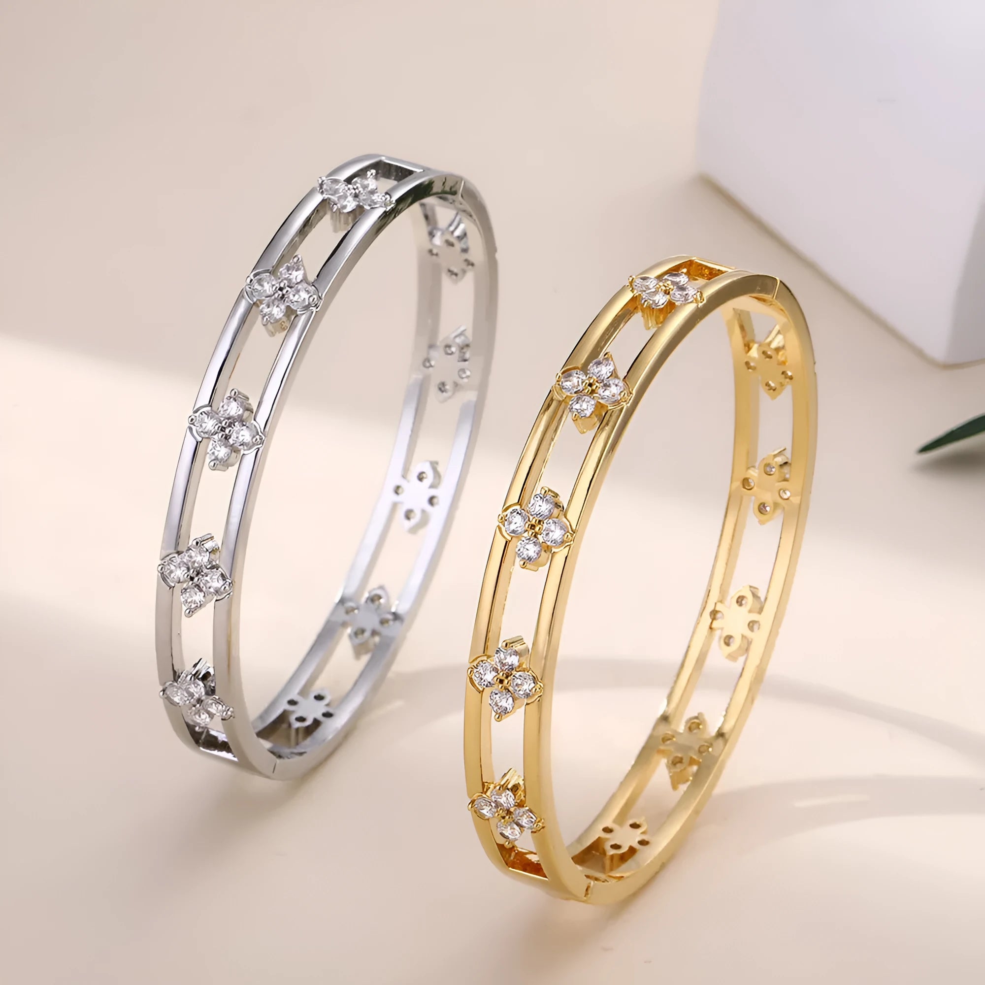 Gold and silver women's hollow bracelets with zircon stones and four-leaf clover charms on a white background.