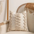 Knitted cushion cover with tassel fringe in a patterned design, shown on a sofa.