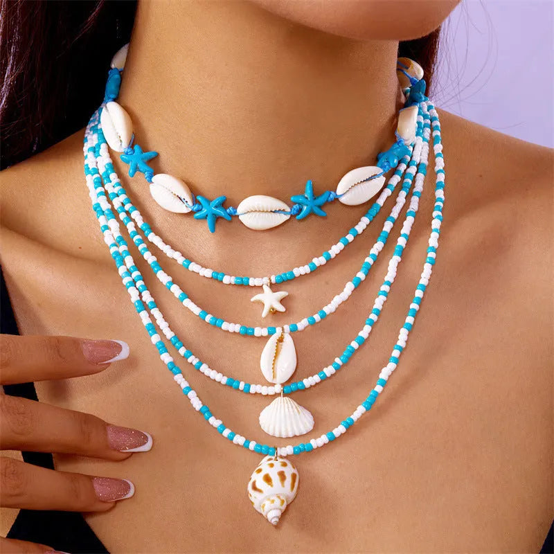Five-piece women's necklace set with blue electroplated starfish, shell, and conch bead pendants on adjustable alloy chains.