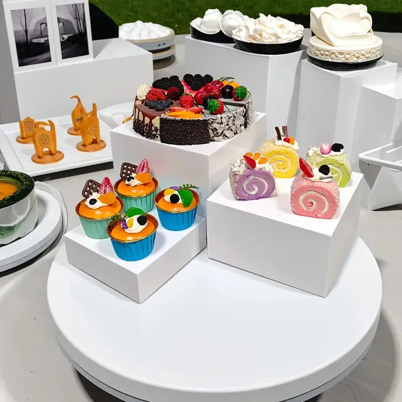 Set of six white plastic cube dessert stands in heights from 3cm to 8cm on a table.