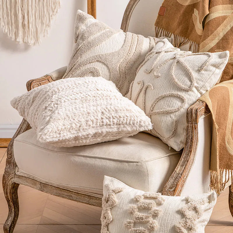 Knitted cushion cover with tassel fringe in a patterned design, shown on a sofa.