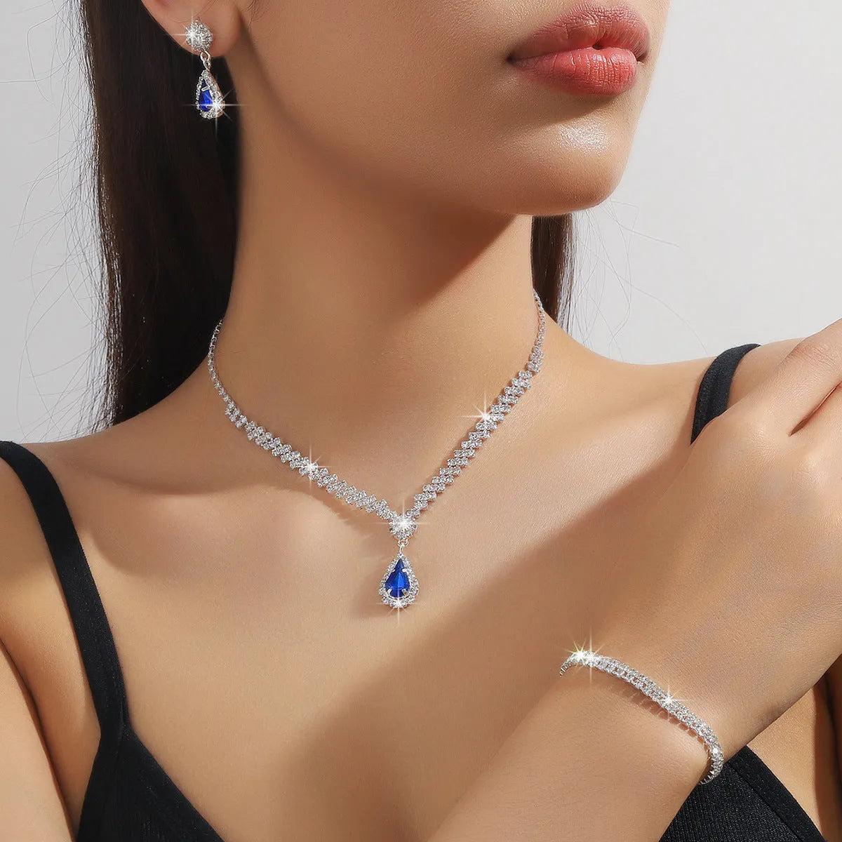 Rhinestone drop pendant necklace and matching earrings with geometric claw chain, shown in blue.