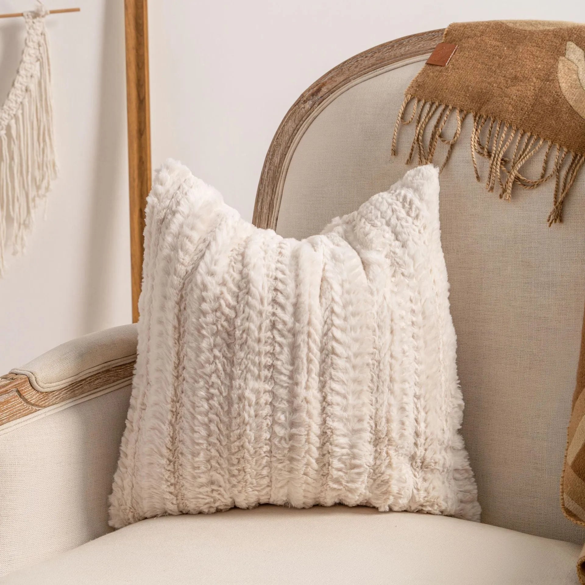 Knitted cushion cover with tassel fringe in a patterned design, shown on a sofa.