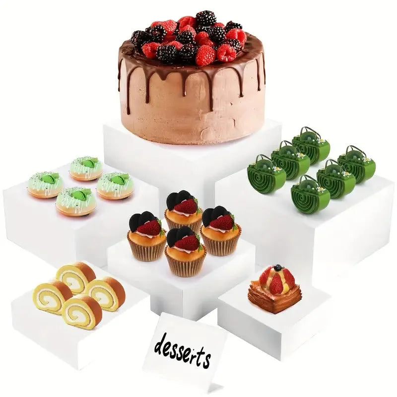 Set of six white plastic cube dessert stands in heights from 3cm to 8cm on a table.