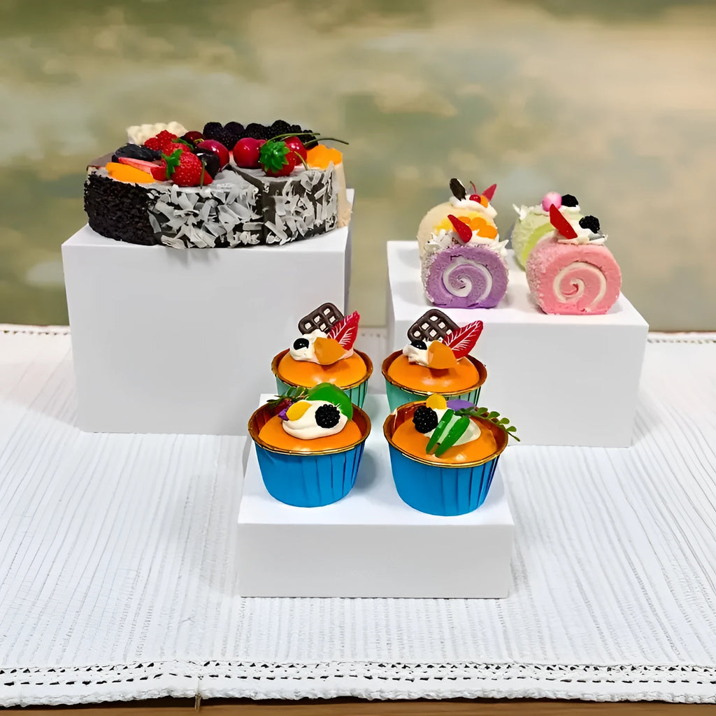 Set of six white plastic cube dessert stands in heights from 3cm to 8cm on a table.