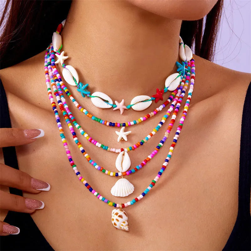 Five-piece women's necklace set with blue electroplated starfish, shell, and conch bead pendants on adjustable alloy chains.