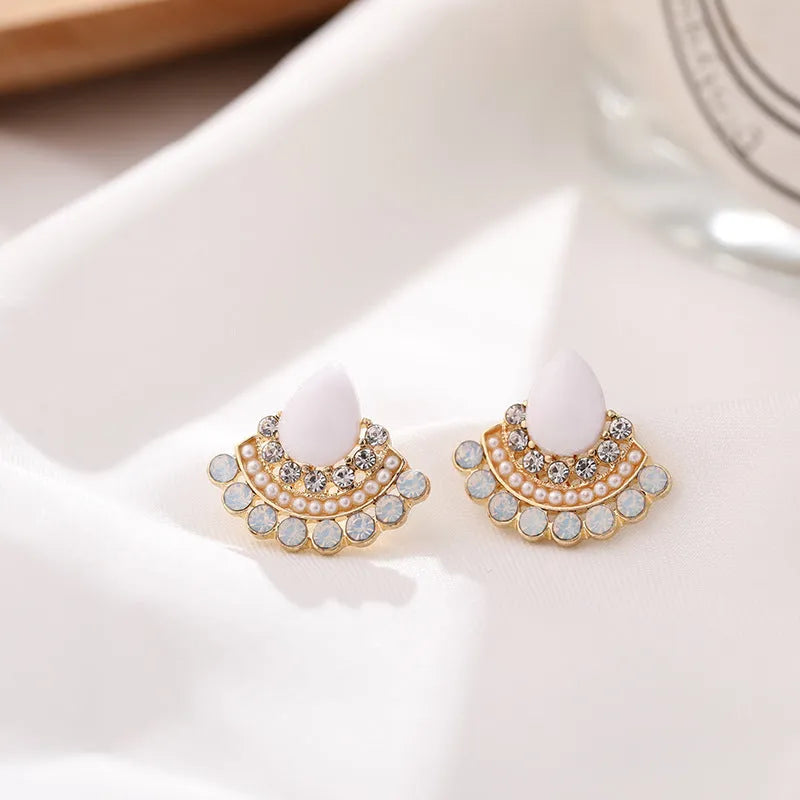 Close-up of silver retro fan-shaped earrings with opal and rhinestone decoration on a needle post.