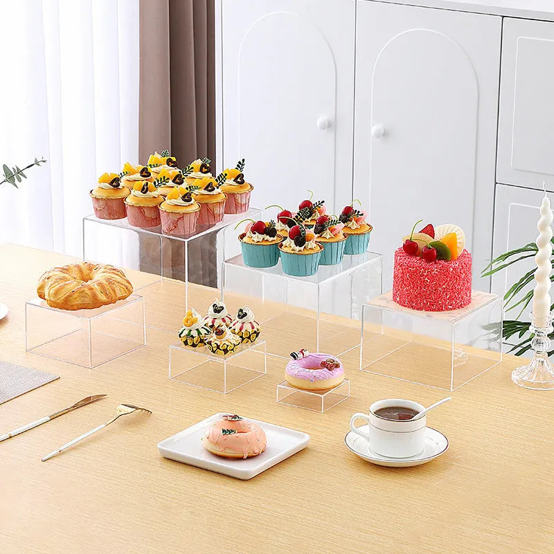 Set of six white plastic cube dessert stands in heights from 3cm to 8cm on a table.