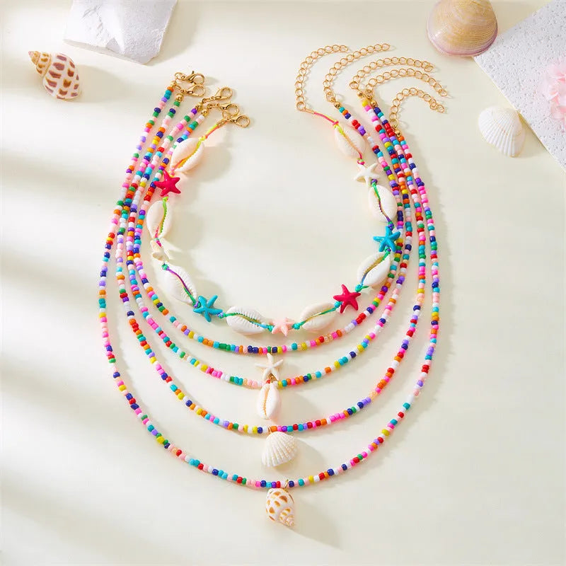 Five-piece women's necklace set with blue electroplated starfish, shell, and conch bead pendants on adjustable alloy chains.