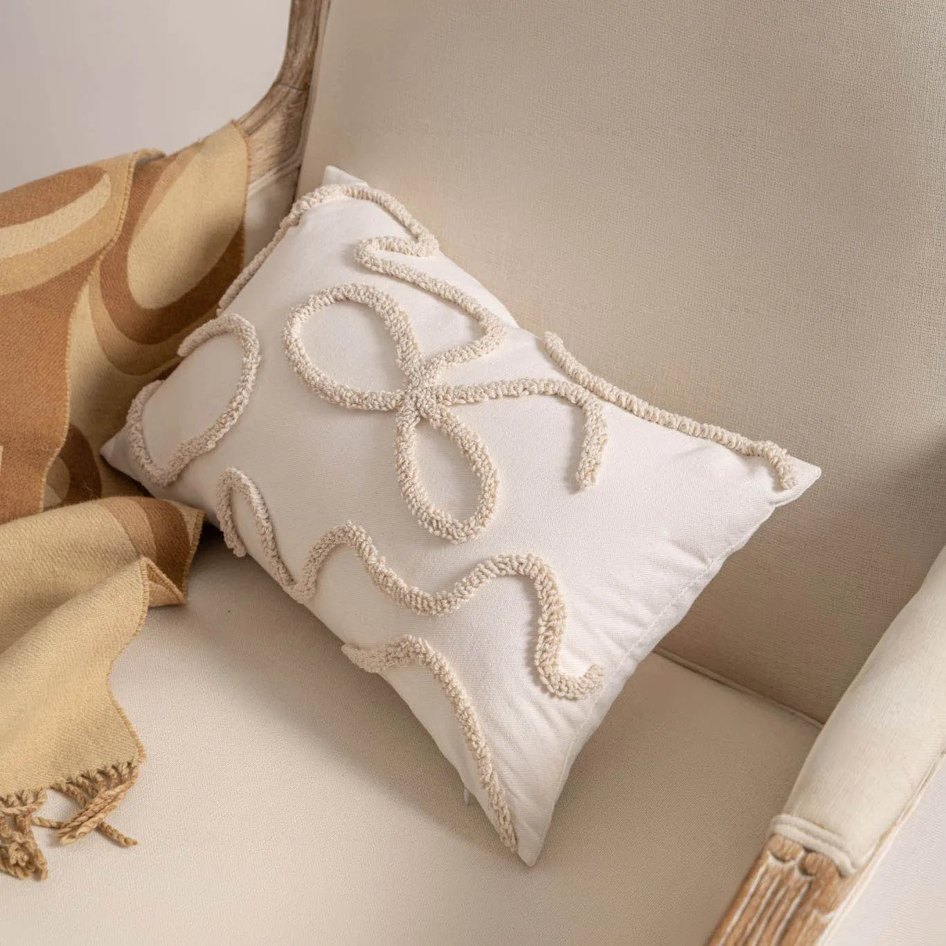 Knitted cushion cover with tassel fringe in a patterned design, shown on a sofa.