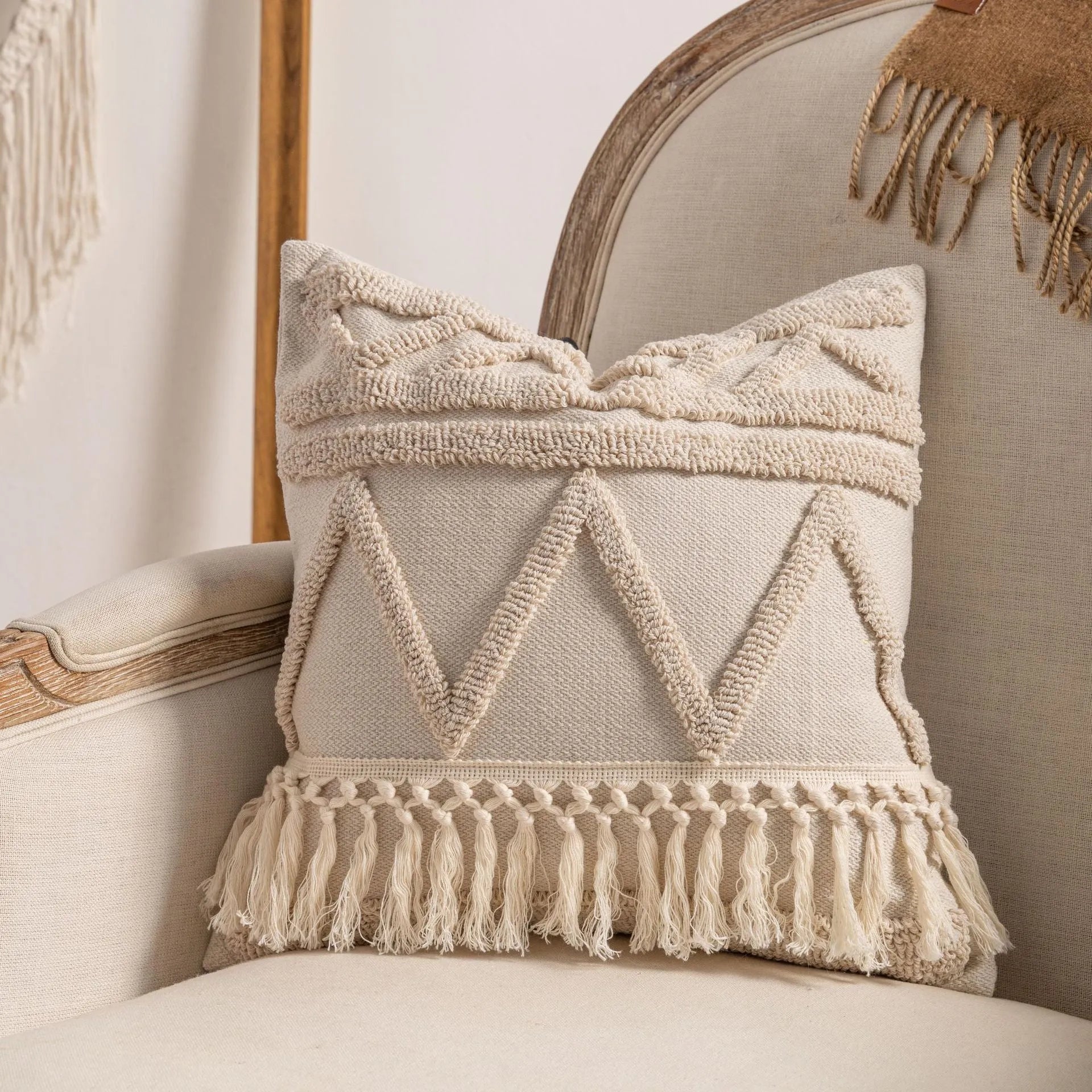 Knitted cushion cover with tassel fringe in a patterned design, shown on a sofa.