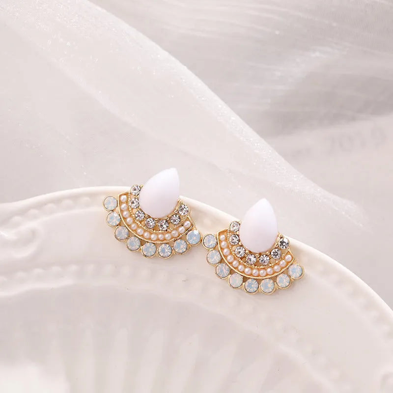 Close-up of silver retro fan-shaped earrings with opal and rhinestone decoration on a needle post.