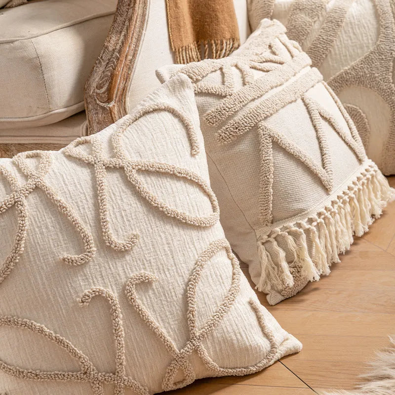Knitted cushion cover with tassel fringe in a patterned design, shown on a sofa.