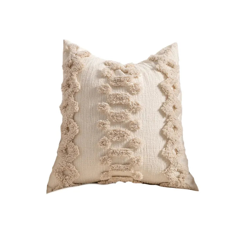 Knitted cushion cover with tassel fringe in a patterned design, shown on a sofa.