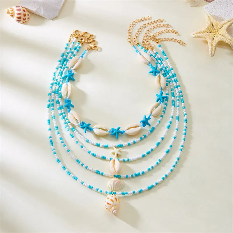 Five-piece women's necklace set with blue electroplated starfish, shell, and conch bead pendants on adjustable alloy chains.