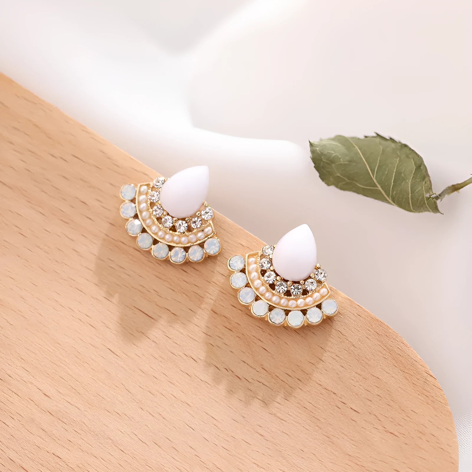 Close-up of silver retro fan-shaped earrings with opal and rhinestone decoration on a needle post.