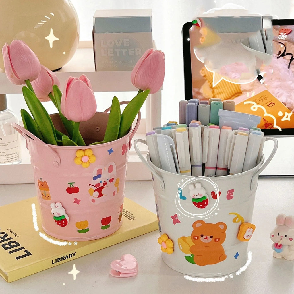 Round metal pen holder in a choice of colours including pink, green, red, white and yellow on a desk.