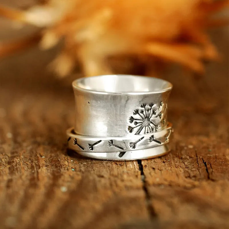 Silver coloured alloy flower ring with rotatable floral detail on a finger.