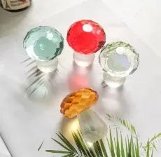 Set of four colourful crystal mushroom decorations in transparent, green, red, and yellow on a white background.