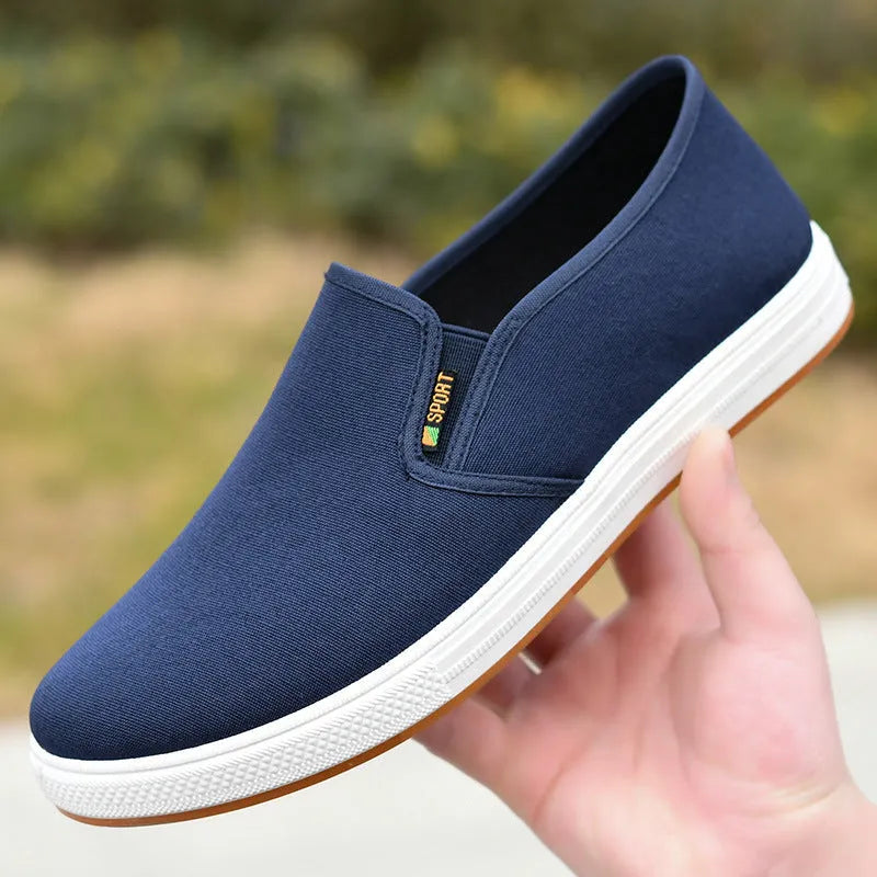Men's low-top slip-on canvas shoe in blue on a white background, showing round toe and shallow mouth design.