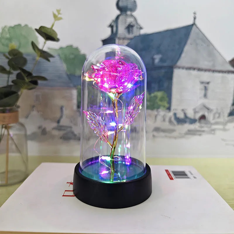 Small decorative table lamp with coloured LED lights illuminating plastic flowers under a glass dome.