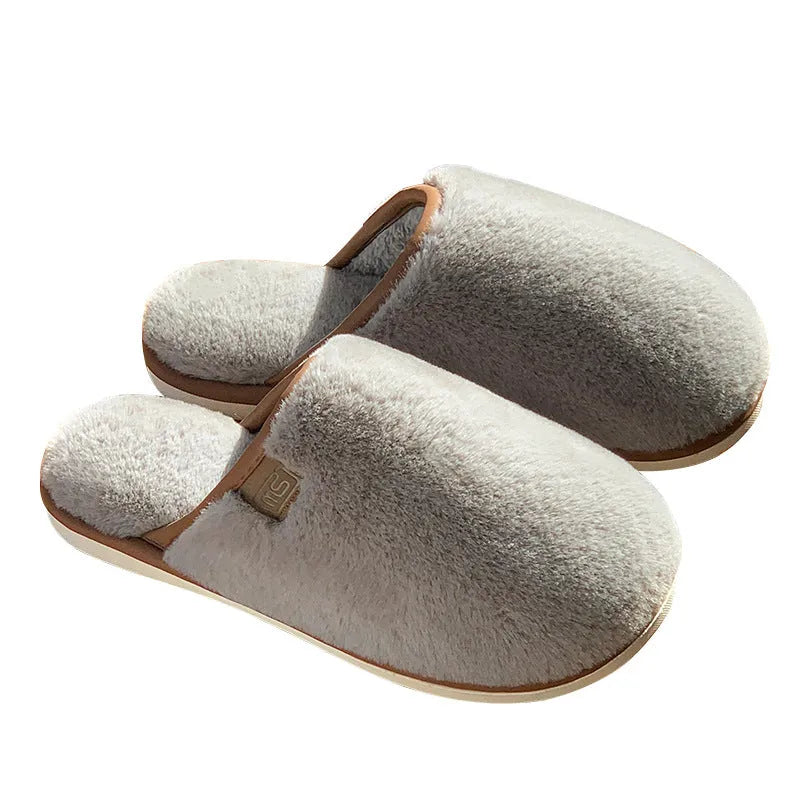 Pair of solid colour plush house slippers with PVC sole on a wooden floor.